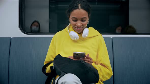 Young Girl Sitting in Metro Looking and Smiling at Phone Wearing Headphones