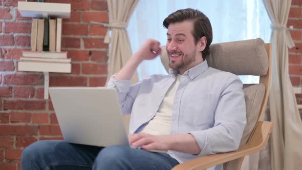 Casual Young Man with Laptop Celebrating Success on Sofa