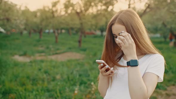 Portrait of a Beautiful Girl Typing on a Mobile Phone While Walking in the Park