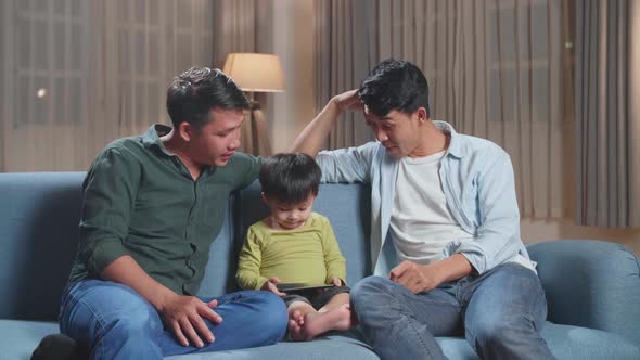 Asian Gay Fathers And Their Cute Son Relaxing On Couch And Using Mobile Phone
