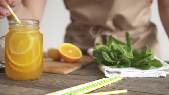 Citrus Lemonade Preparation At Home. Lady In The Apron Prepares A Drink With Slices Of Lemon, Orange