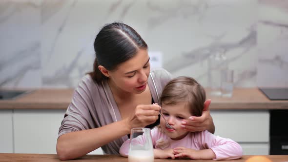 Lovely Mother Feeding Daughter Natural Yogurt at Home Kitchen