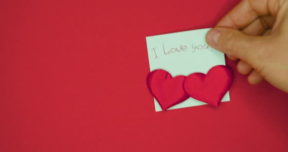 Male Hand is Pasting Sticker with the Words I Love you Written in Pen and Pasted Two Hearts for