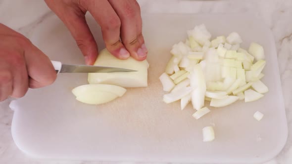 Closeup of a mans hand cutting up the onions on a white board with a steel knife. Home cooking conce
