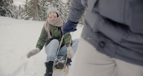 Slow Motion Portrait of Happy Asian Woman Riding Sled Laughing Talking to Boyfriend in Winter Forest