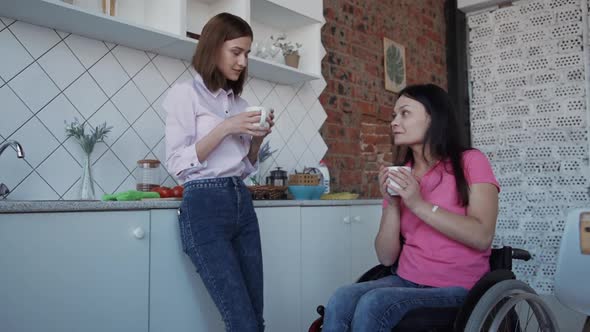 Woman in Comfort Wheelchair Holding Cup in Hands and Talking Wit