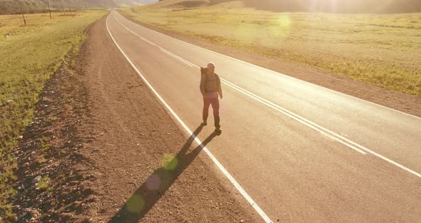 Flight Over Hitchhiker Tourist Walking on Asphalt Road. Huge Rural Valley at Summer Day. Backpack