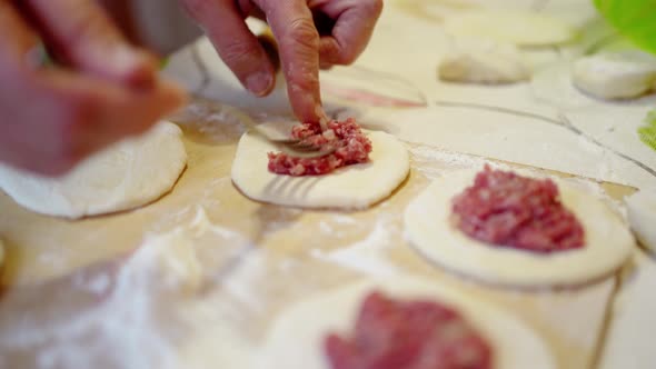 Female Hands with a Fork Put the Meat Filling Into a Round Rolled Out Dough