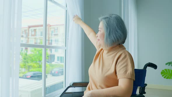 Asian Senior older disabled woman sit on wheelchair and open window feel happy and enjoy sunrise.