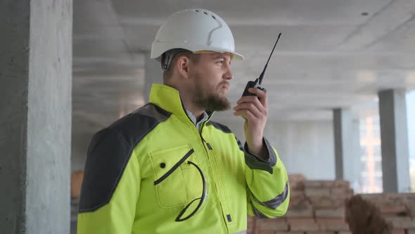 Architect Builder Talking on The Radio Building Under Construction. Engineer in White Hard Hat