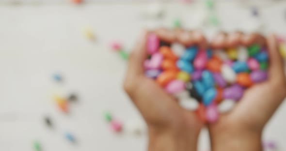 Video of overhead view of biracial man holding multi coloured sweets over white rustic background