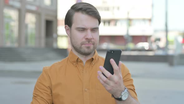 Young Man Celebrating Online Success on Smartphone Outdoor