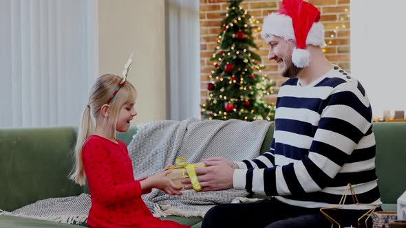 Father gives a Christmas gift to his daughter dressed in festive red dress