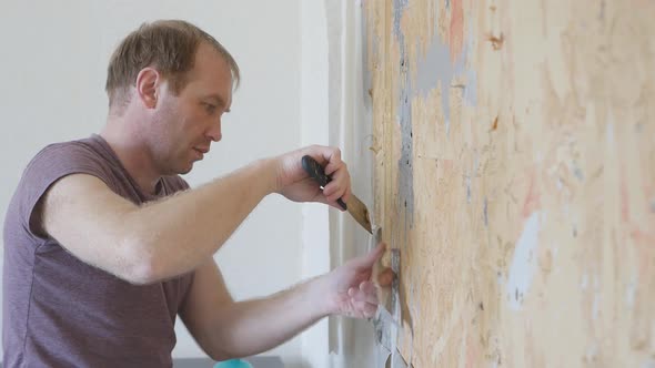 A Young Man Removes Old Wallpaper From the Wall with a Spatula