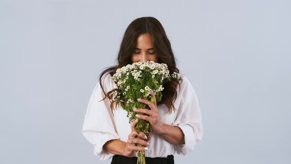 Brunette Model in White Shirt is Holding a Bouquet of Chamomile Flowers Sniffing It and Enjoying Its