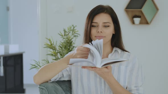 Portrait of pretty young brunette woman smiling and flipping the book at home