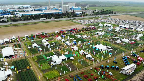 Drone Shot with Curved Revealing Top View of Agricultural Expo Fair on Green Fields of Farm Lands wi