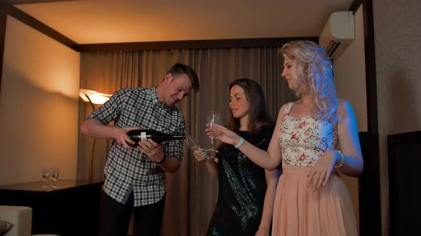 Young Guy Pouring Champagne in Glasses of Two Sexy Ladies.