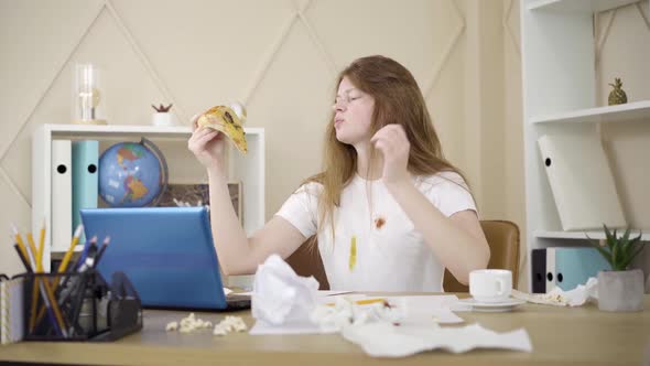 Young Woman Scratching Head and Eating Pizza As Sitting in Front of Laptop