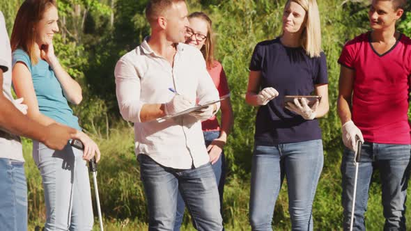 Mid adults volunteering and taking notes and using a tablet during river clean-up day