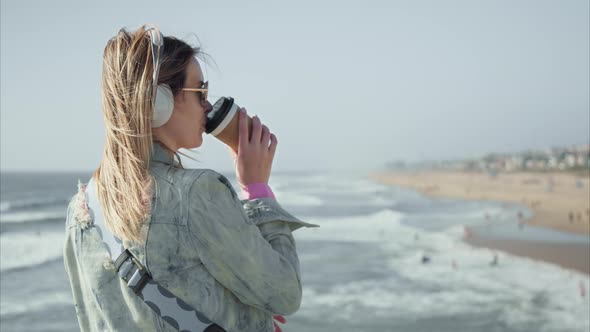 Beautiful Woman on Ocean Pier with Great Landscape Views Drinking Coffee or Tea