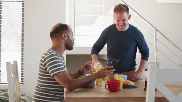 Multi ethnic gay male couple having breakfast and talking one using smartphone