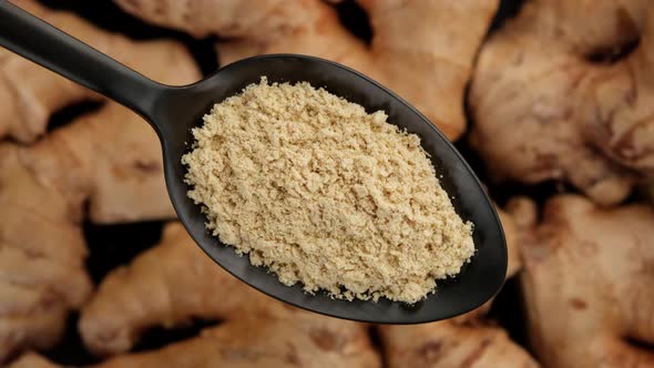 ground ginger in spoon and whole ginger root on background rotating.  top view