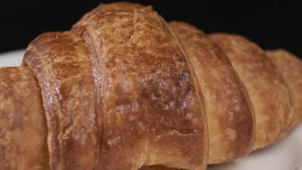 Croissant on white plate rotating in front of camera on black background