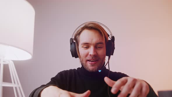 Portrait of Young Caucasian Man with Headphones Laughing Speaking and Typing on the Laptop Keyboard