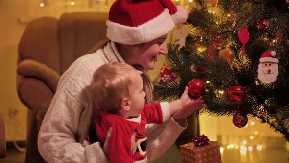 Little Baby Boy with Mother in Santa Claus Hat Decorating Christmas Tree with Baubles