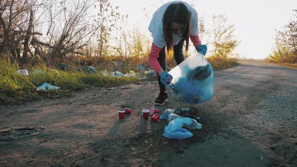 Volunteer Woman Picking Up Trash and Plastics Cleaning the Park with a Garbage Bag. People and