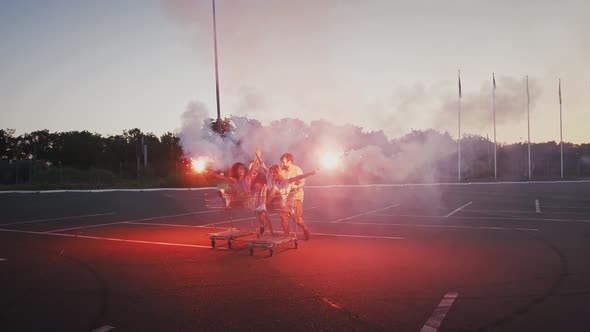 Young Friends Riding on Shopping Trolleys at Deserted Parking Lot of Hypermarket Holding Burning