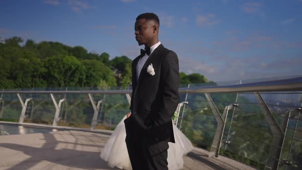 Frustrated African American Groom in Elegant Suit on Summer Bridge with Sad Bride Leaving in Slow