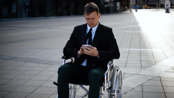 Young Business Man Sitting on Wheelchair Is Playing or Working with His Smartphone