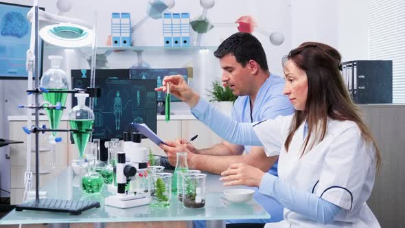 Scientists with Her Assistant Looking at Test Samples with Green Liquid alt