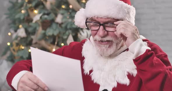 Santa Claus in Eyeglasses Reading Letters and Smiling, Old Caucasian Man in Christmas Costume