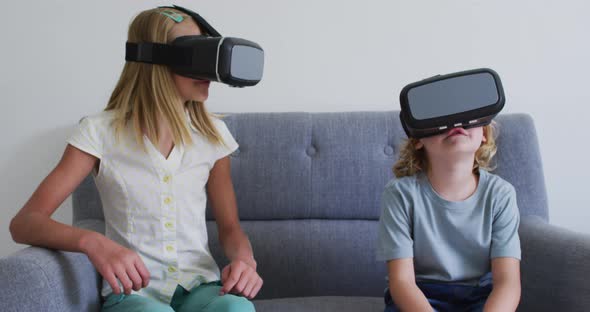 Caucasian brother and sister gesturing while using vr headset sitting on the couch at home