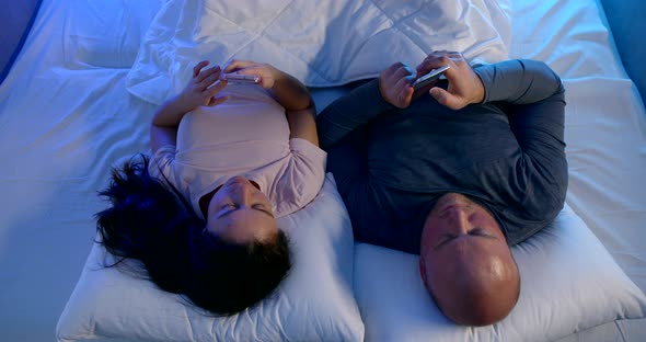 Adult Man and Woman Are Lying in Bed and Using Internet in Smartphones Before Sleep at Night