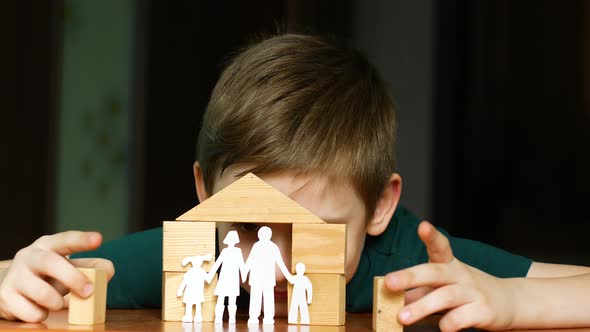 Caucasian boy 7 years old plays with wooden cubes builds a house, the child cut out a family from pa