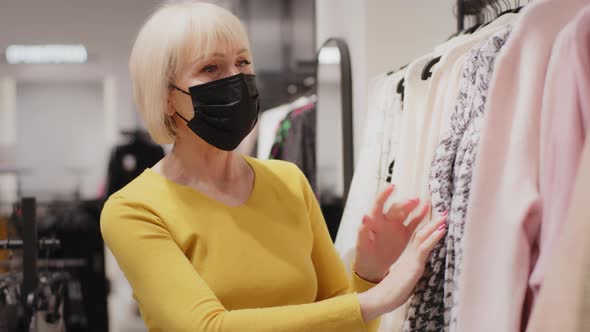 Elderly Woman Buyer in Protective Mask Chooses Clothes in Boutique Looking for New Outfit Happy