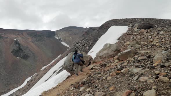 Male hiker climbing on rocky slope of Mount Asahidake in Japan during cloudy day