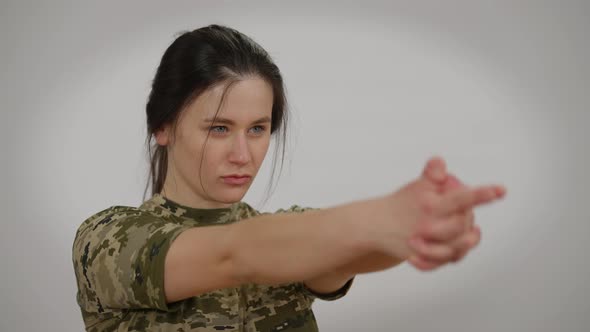 Focused Millennial Woman in Khaki Tshirt Imitating Gun Shooting with Hands Gesturing Blowing Turning