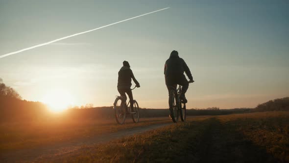 Couple Tourists Ride on Bike on the Road. Two Silhouettes of Cyclists on a Sunset Background. Sport