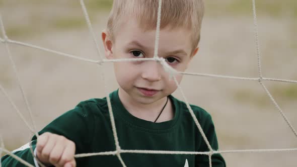 A Sad Boy Looks at the Camera is Behind a Rope Net