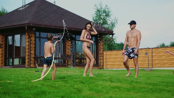 Family in the Backyard of a Country House in the Summer Relax Playing with Water and Hosing