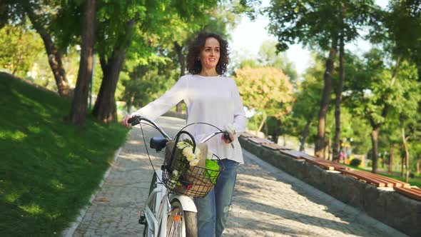 Smiling Attractive Woman in a White Tshirt and Blue Jeans Walking Holding Her City Bicycle's