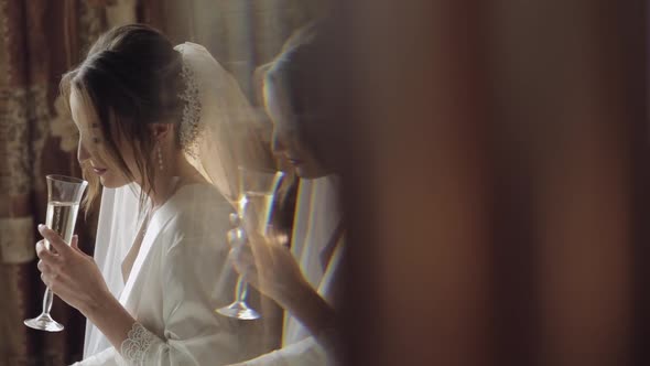 Beautiful and Lovely Bride in Night Gown and Veil Sitting and Drinking Champagne