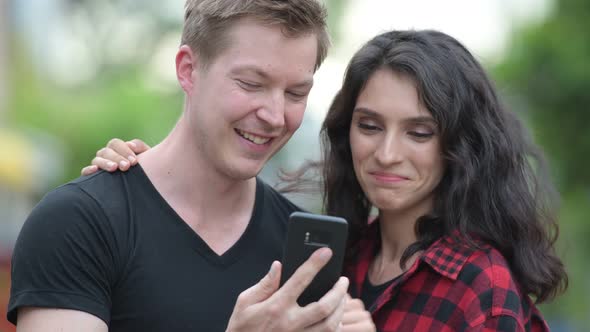 Young Couple Using Phone Together Outdoors