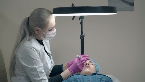 Professional Cosmetician Holds Tattoo Gun and Lady Forehead