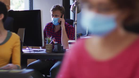 Caucasian man wearing face mask talking on smartphone at modern office